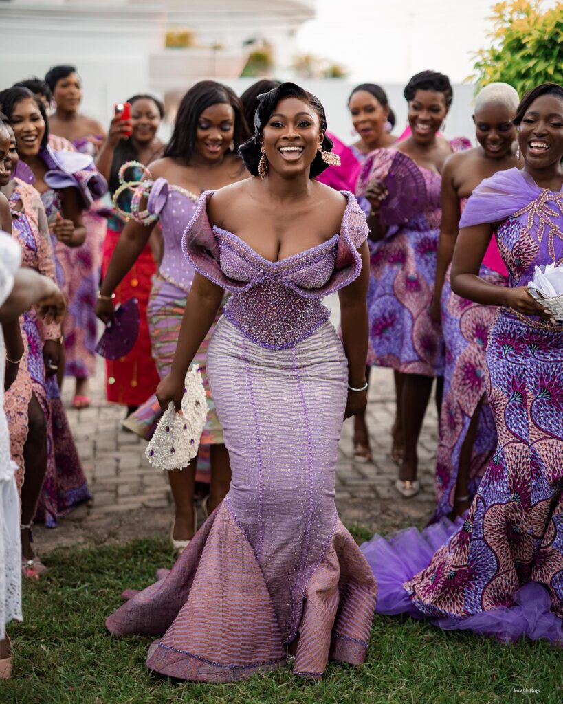 A bride in her two piece engagement kente dancing with her bridesmaids