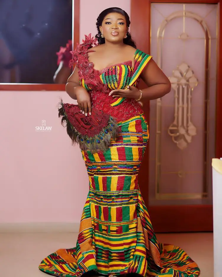 A beautiful bride in her wedding engagement kente dress holding a bridal fan and posed for the camera