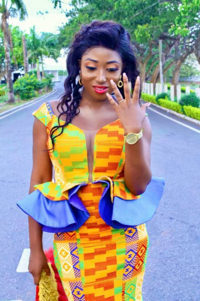 A Ghanaian bride in an engagement kente outfit without beads holding a bridal fan