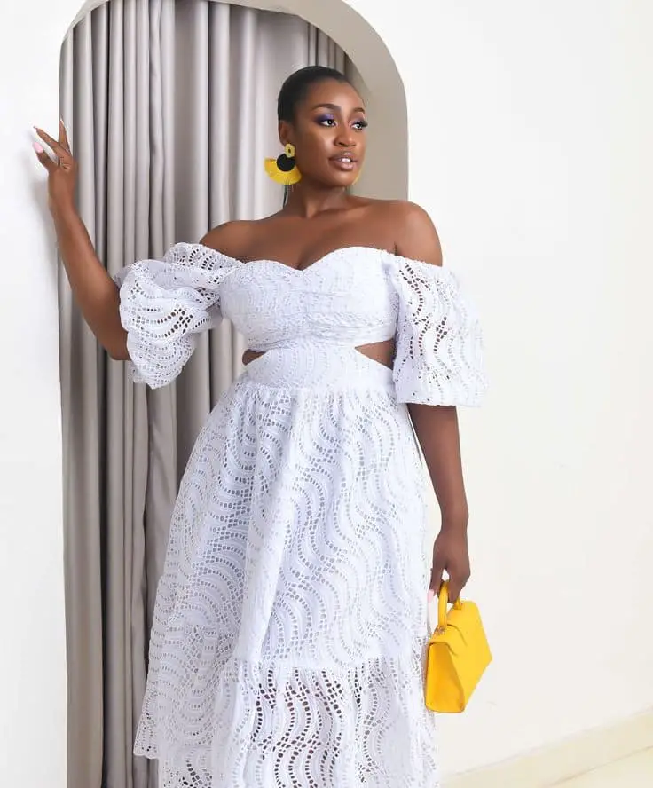 A lady in a wedding guest white lace dress and yellow bag and earrings styles in Ghana 